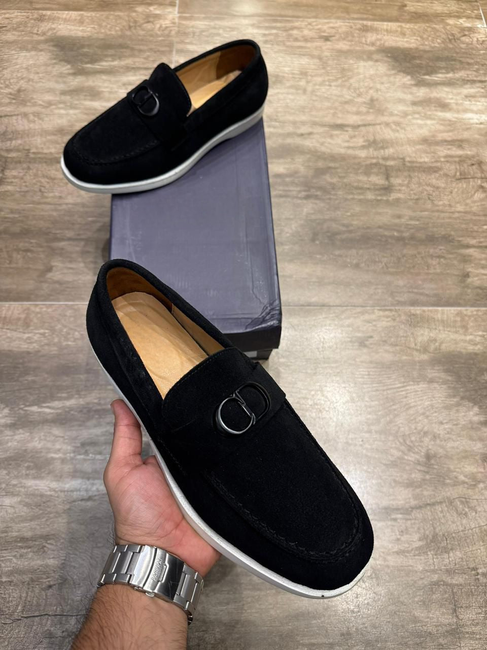 Close-up of black suede loafers with metal buckle and tan leather lining.