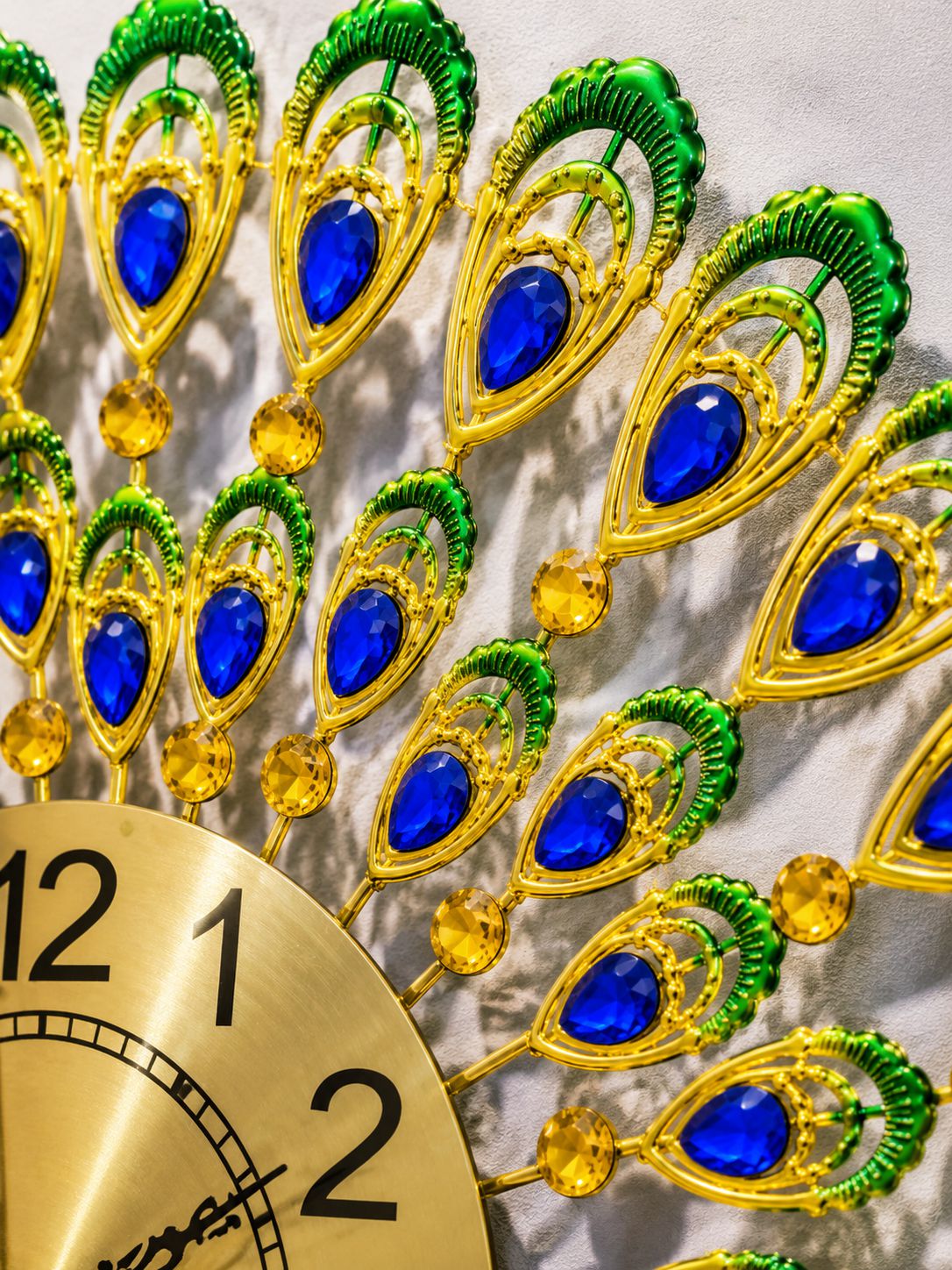 Close-up of blue crystal peacock feather accents on decorative metal wall clock
