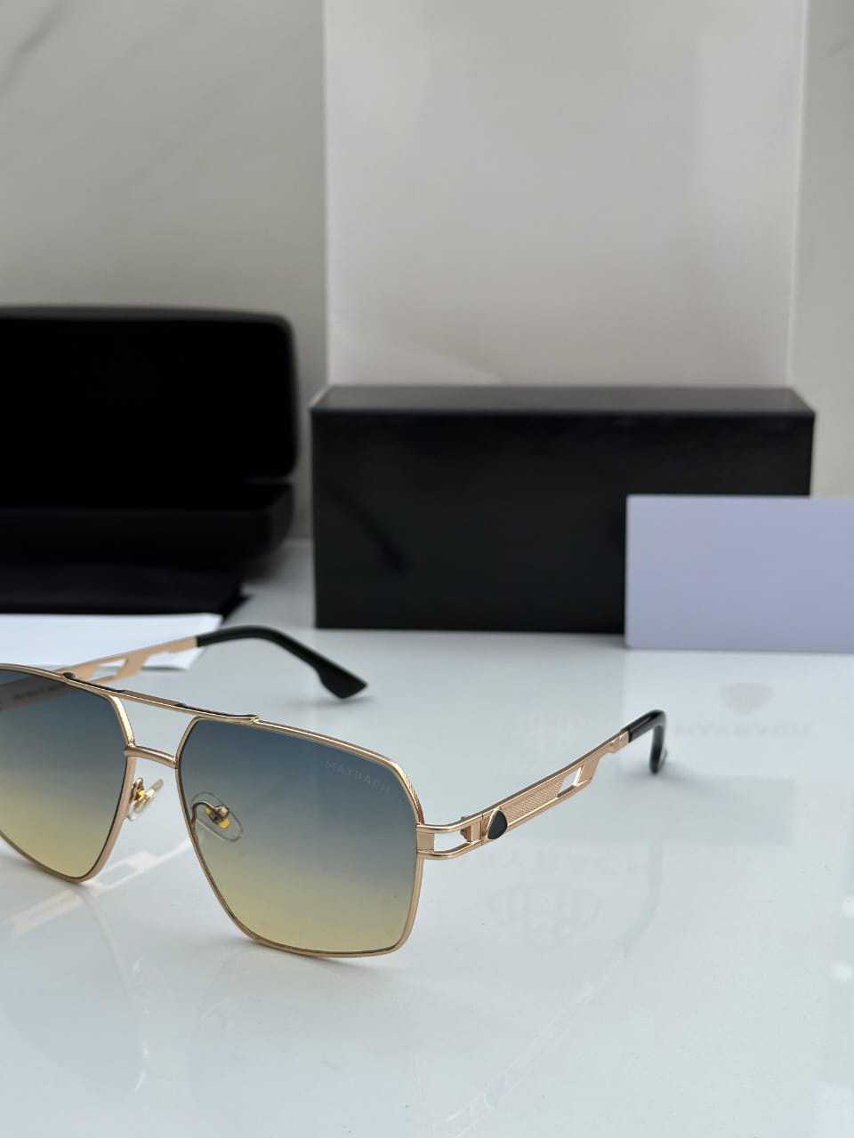 Close-up of gold metal hexagonal aviator sunglasses with yellow-to-blue gradient lenses.