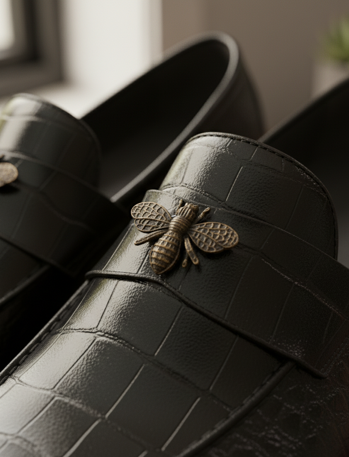 Close-up of the antique gold bee metal detail on the black crocodile-embossed faux leather loafer.