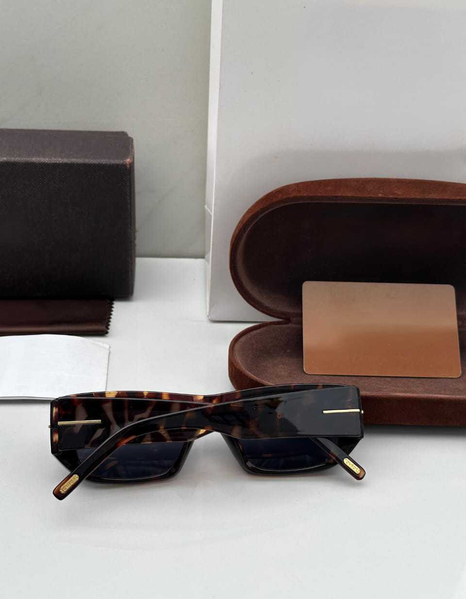 Close-up of premium tortoiseshell rectangle sunglasses with gold 'T' temple accents.