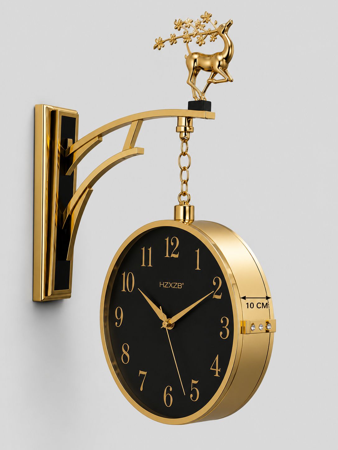 Gold wall-mounted decorative clock with a black dial, gold numerals and hands, a hanging chain, and a deer figurine on top, shown against a light gray background.