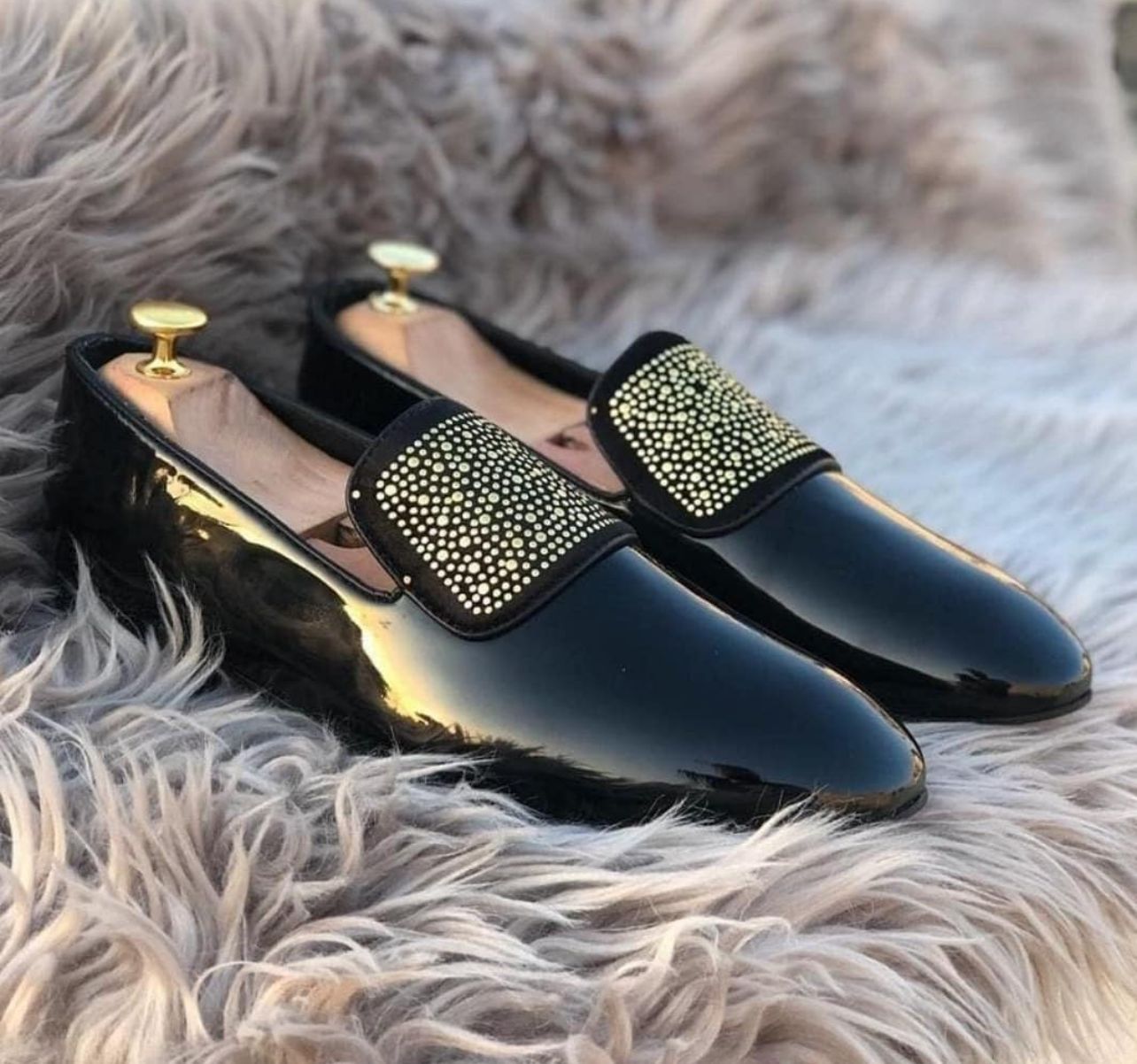 A pair of black studded suede loafer shoes displayed on a furry surface.