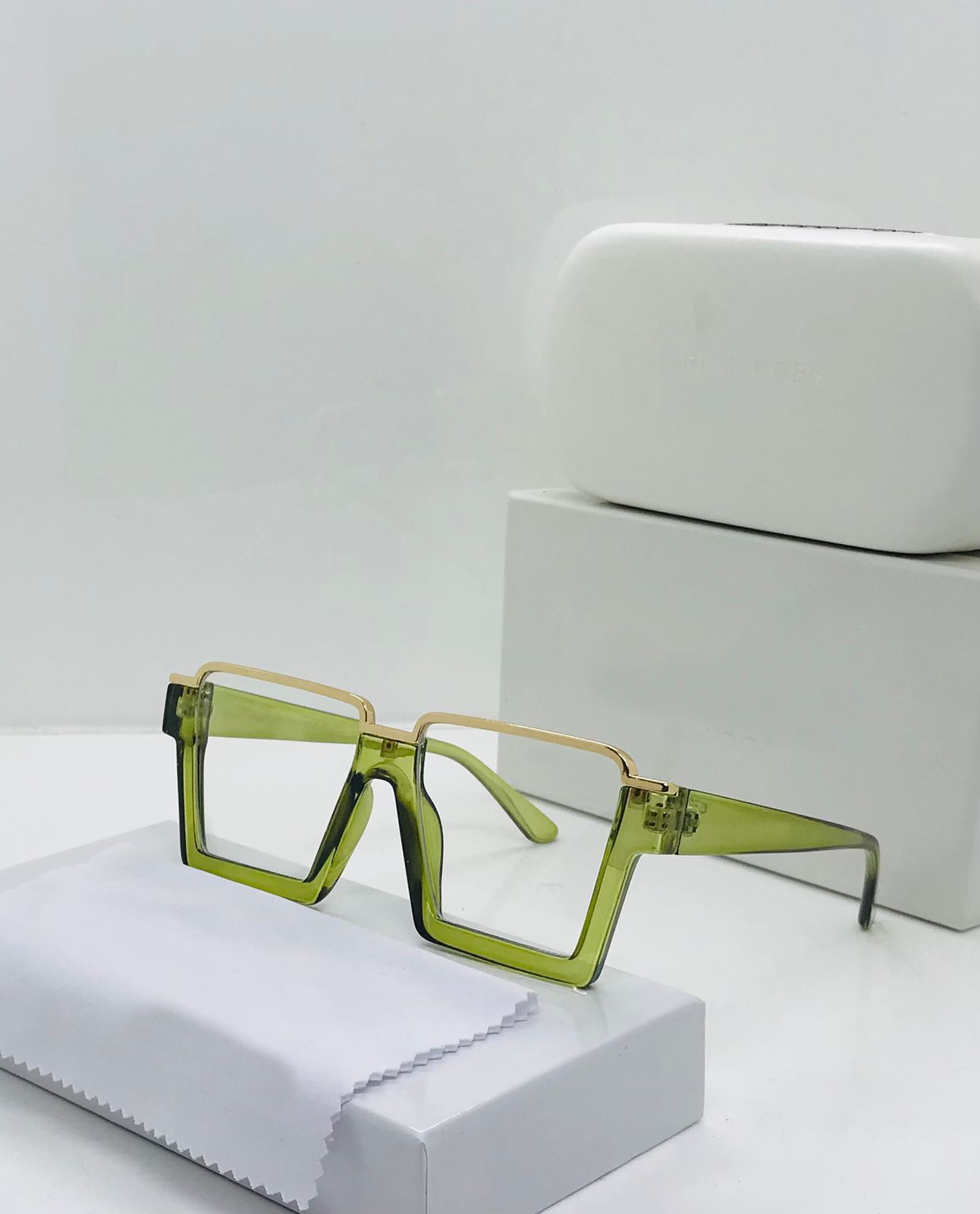 Green square-framed glasses on a white surface with a white box in the background