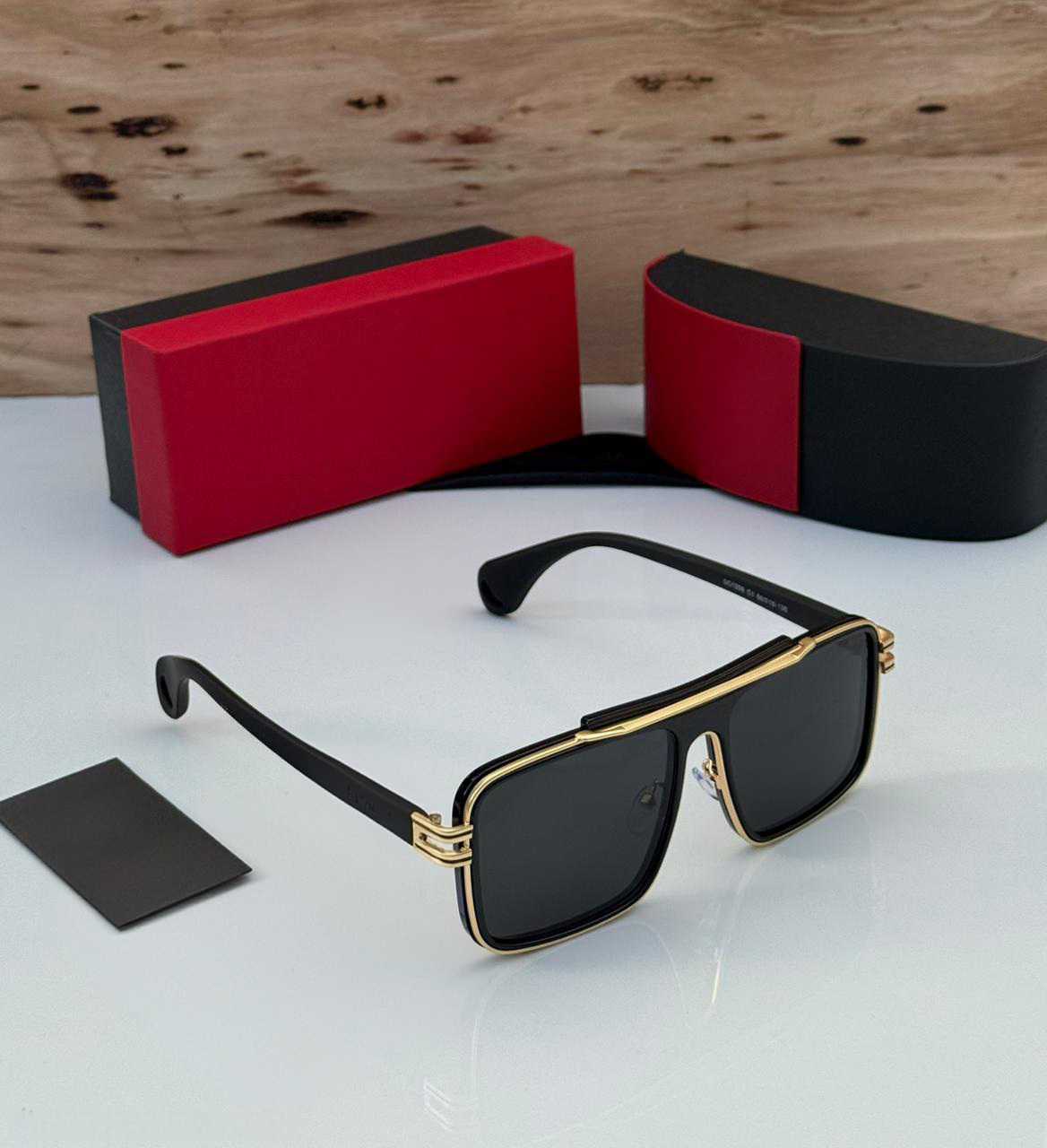 Hand holding black and gold oversized square aviator sunglasses with dark lenses.