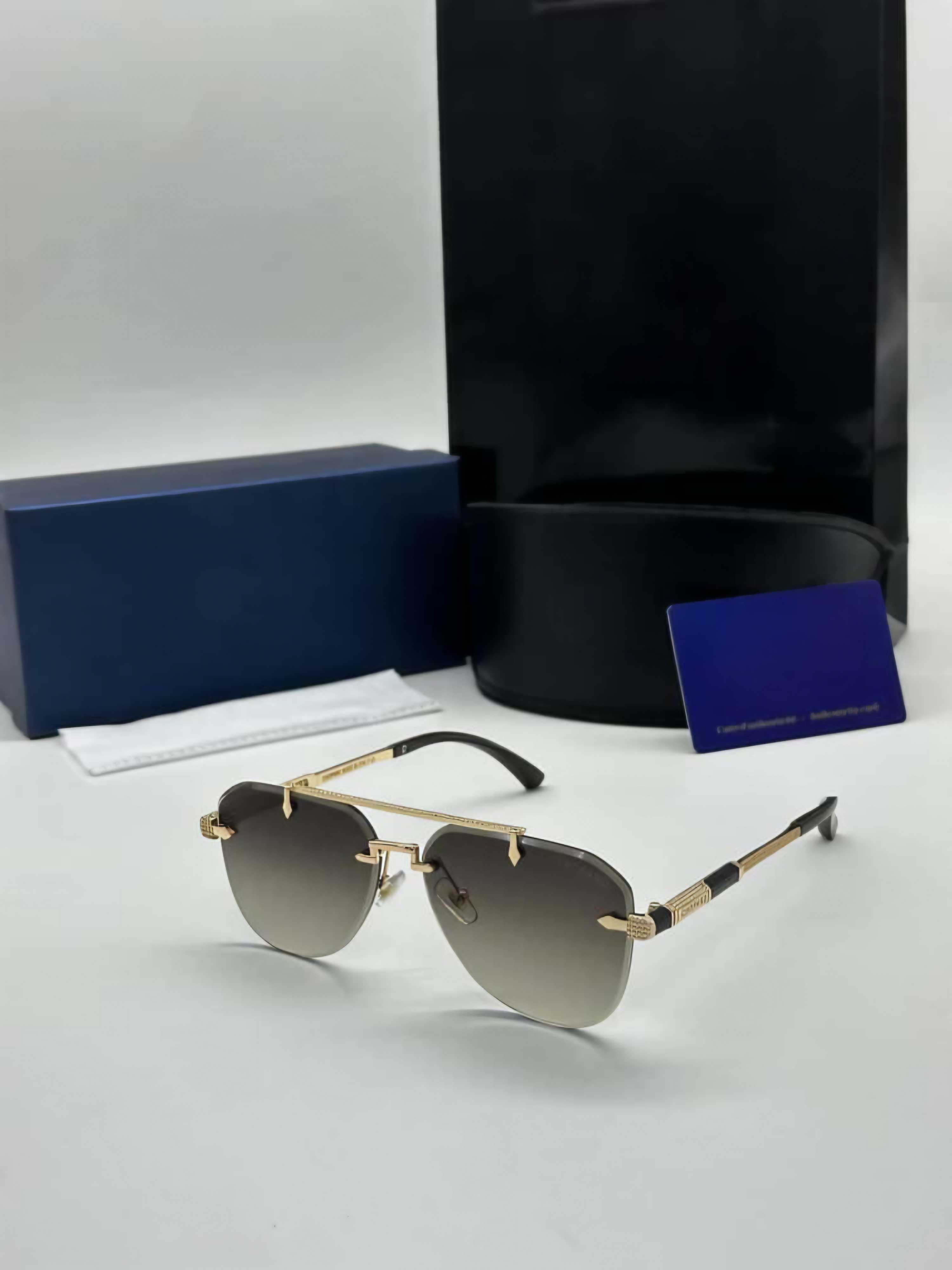 Luxury rimless aviator sunglasses with gold metal frame and brown gradient lenses, displayed with blue and black packaging.