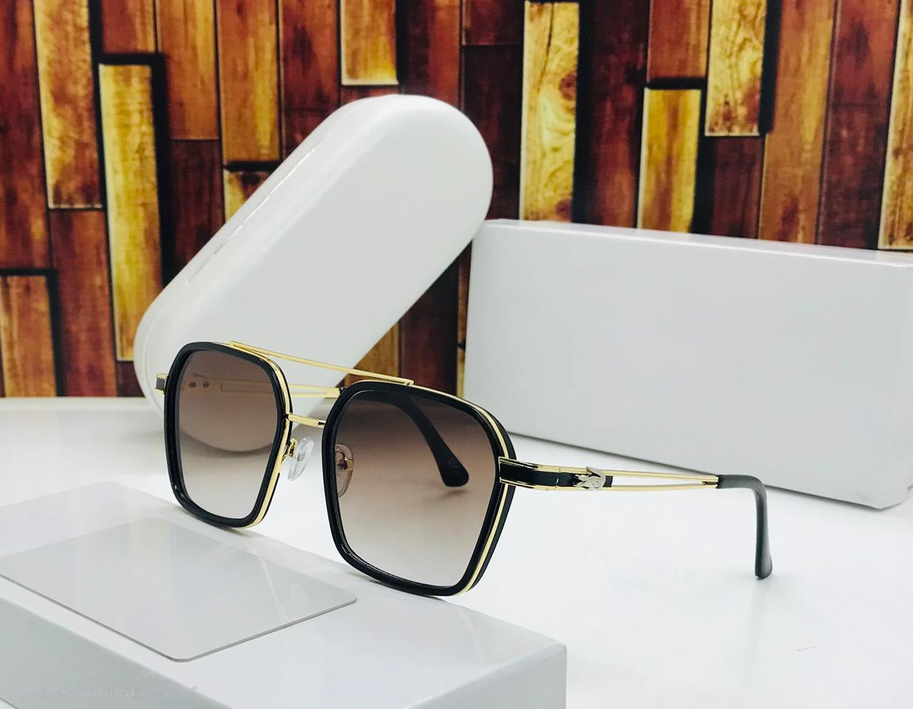 Men's stylish square sunglasses with black and gold frame and brown gradient lenses next to white case.