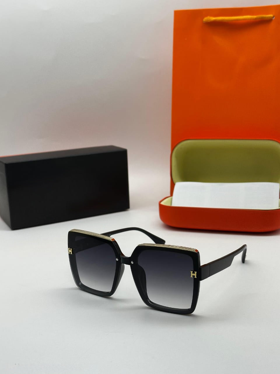 Oversized black square sunglasses with gold trim and H-logo detail on the temples and grey gradient lenses