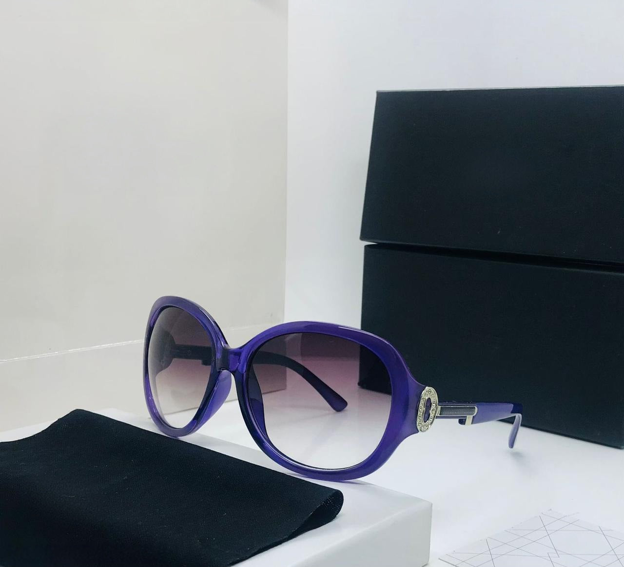 Oversized bright purple round sunglasses with dark gradient lenses and a large gold metal/jewel accent on the temple.