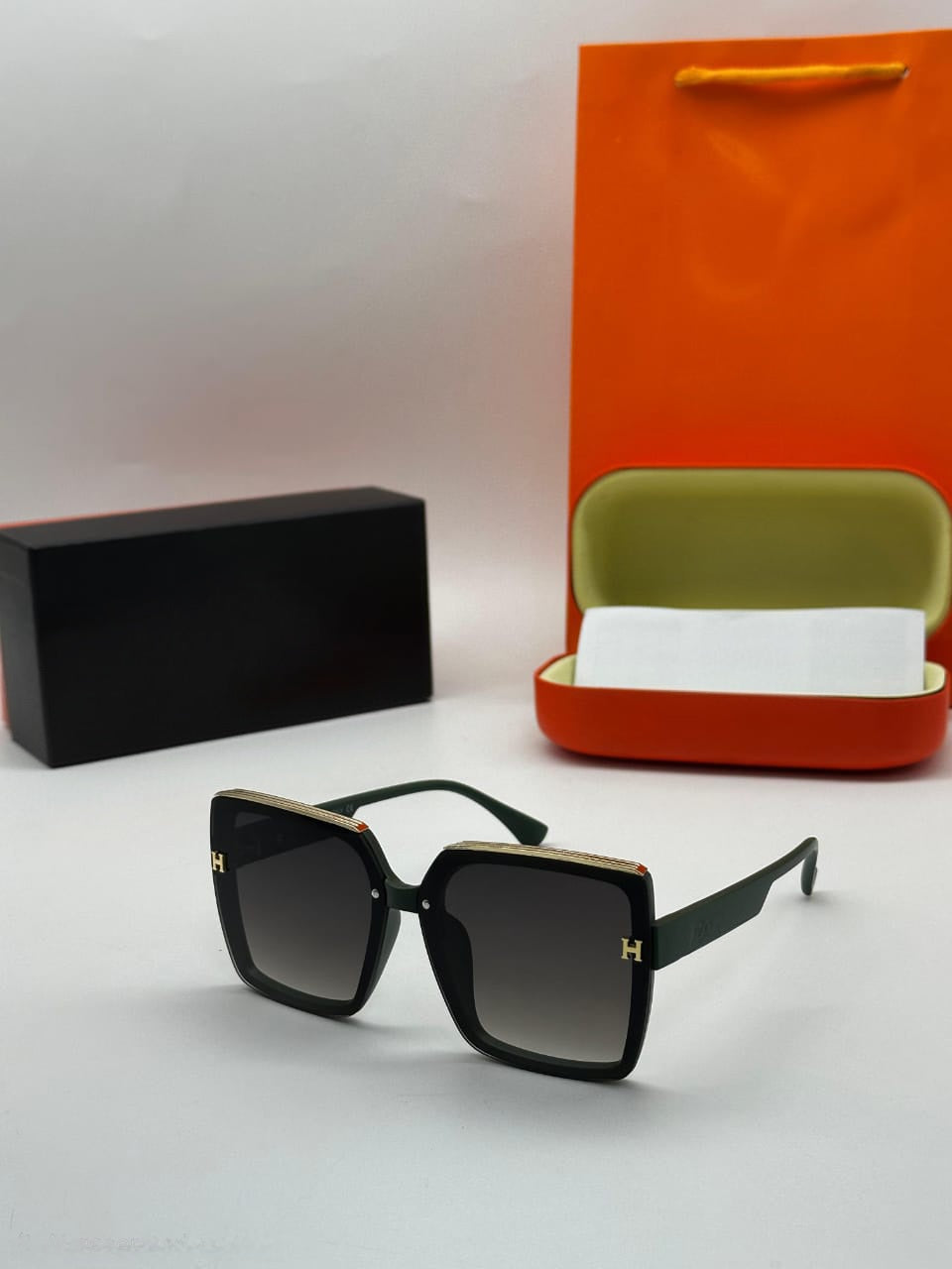 Oversized dark green square sunglasses with gold trim and H-logo detail and dark gradient lenses.