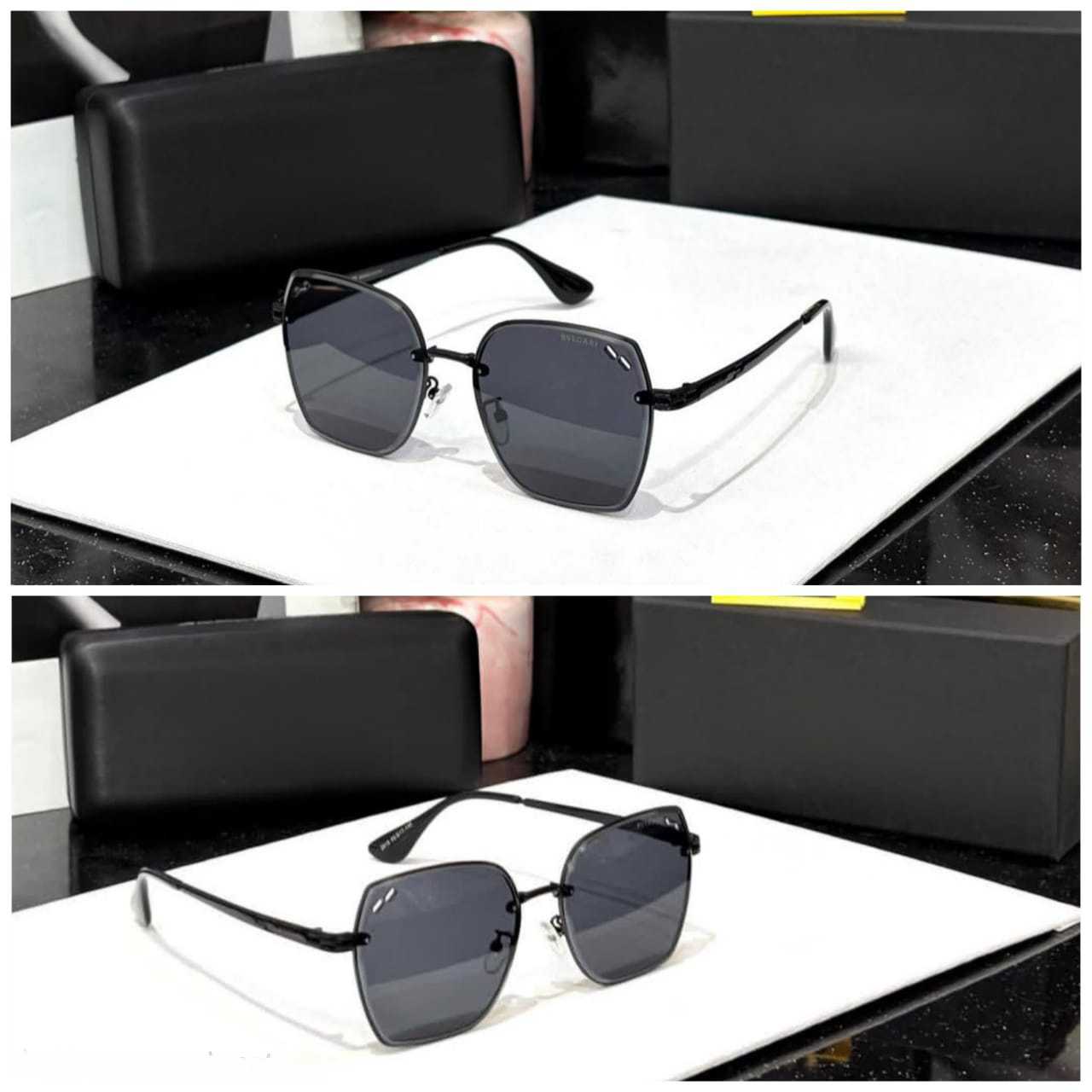 Oversized hexagonal sunglasses with a thin black metal frame and dark lenses, displayed on a white surface with black packaging