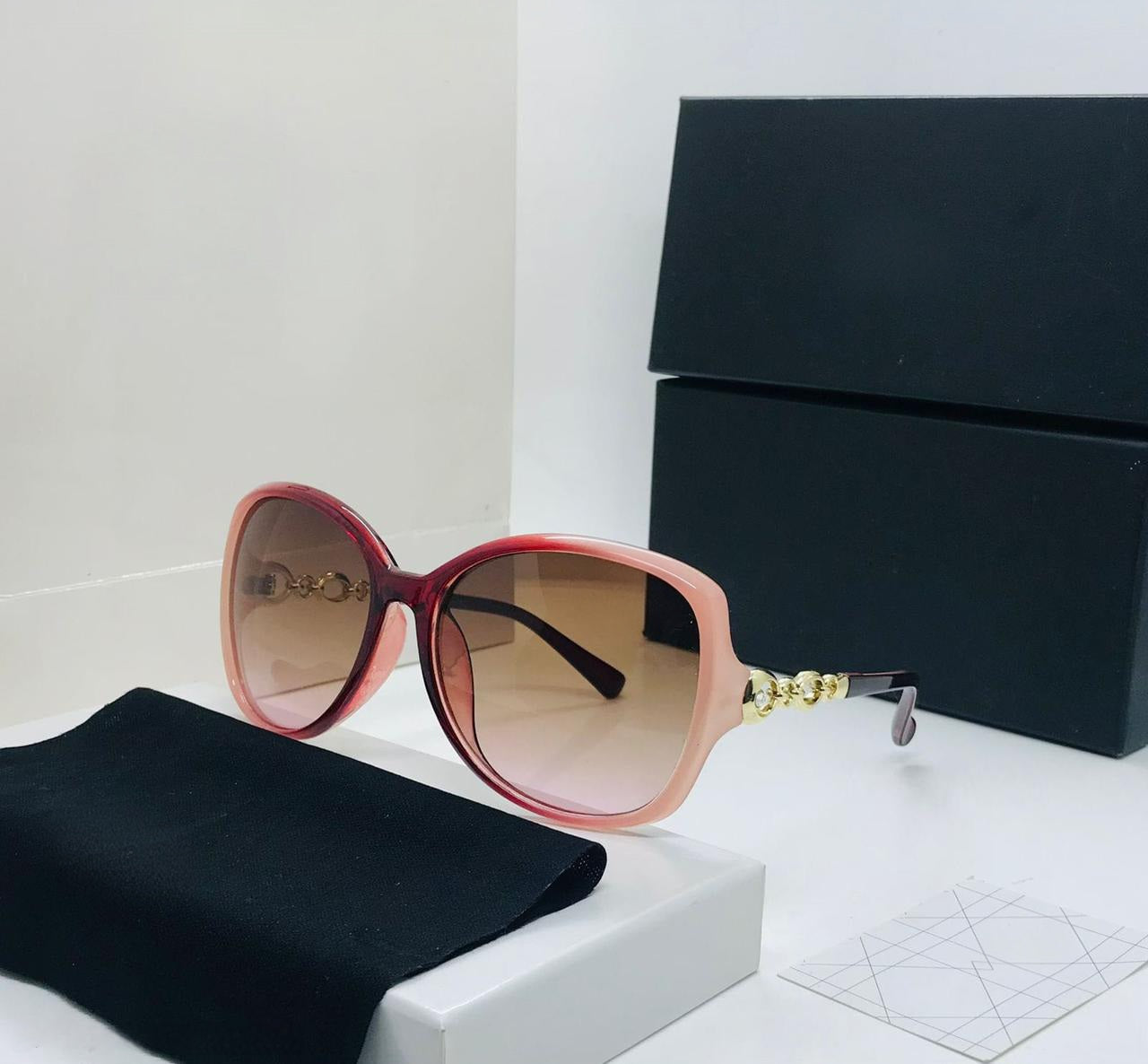 Oversized pink and burgundy ombre sunglasses with brown gradient lenses and gold chain link detail on the temple.