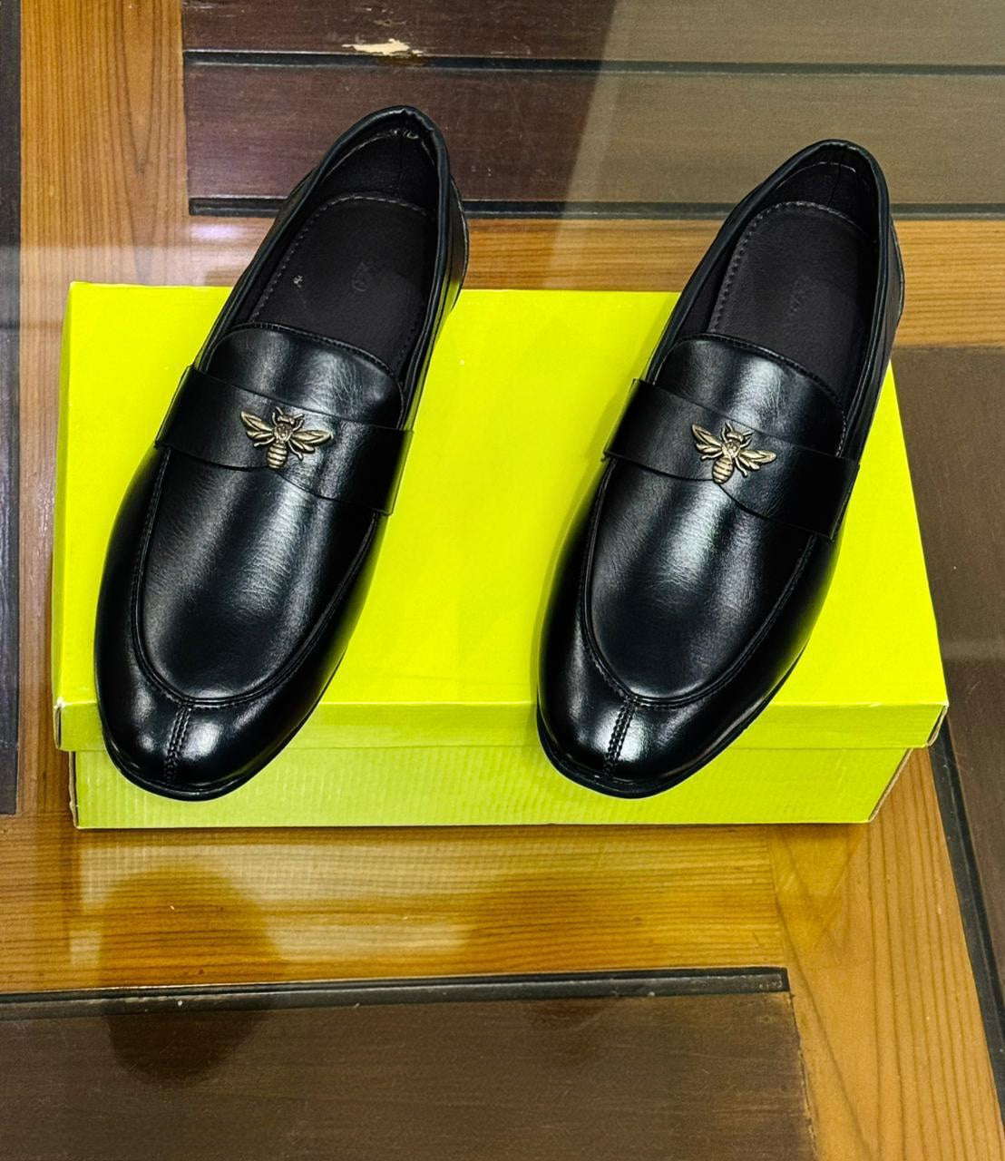 Pair of black slip-on shoes with bee buckle on yellow FunkyTradition box