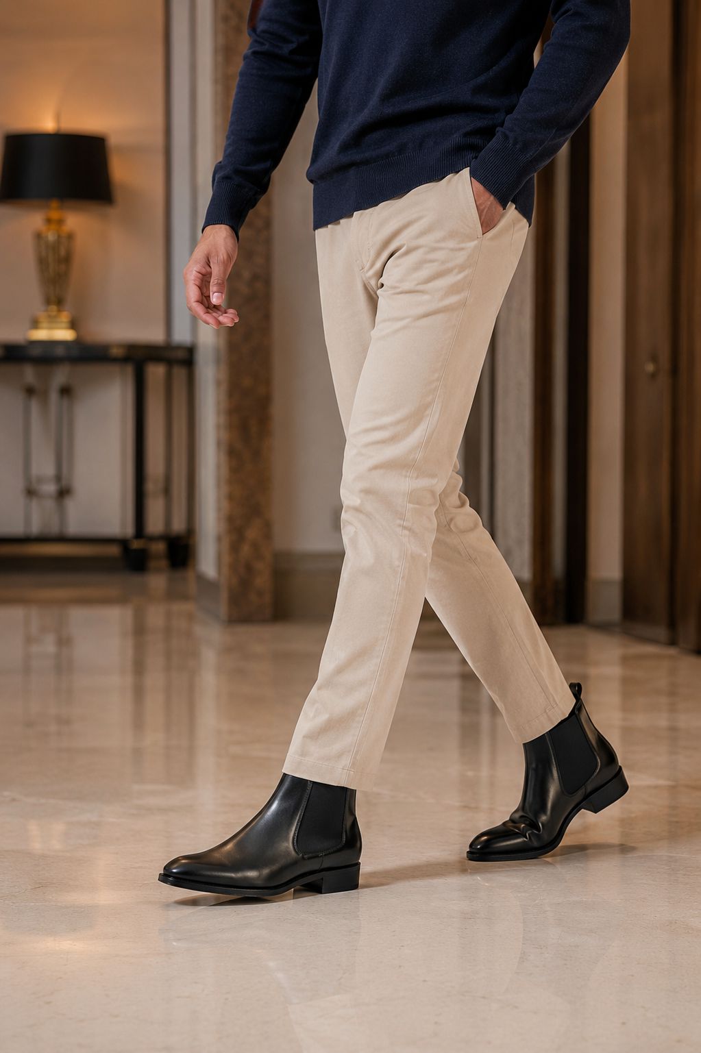 Person wearing beige pants and black Chelsea boot shoes in an indoor setting