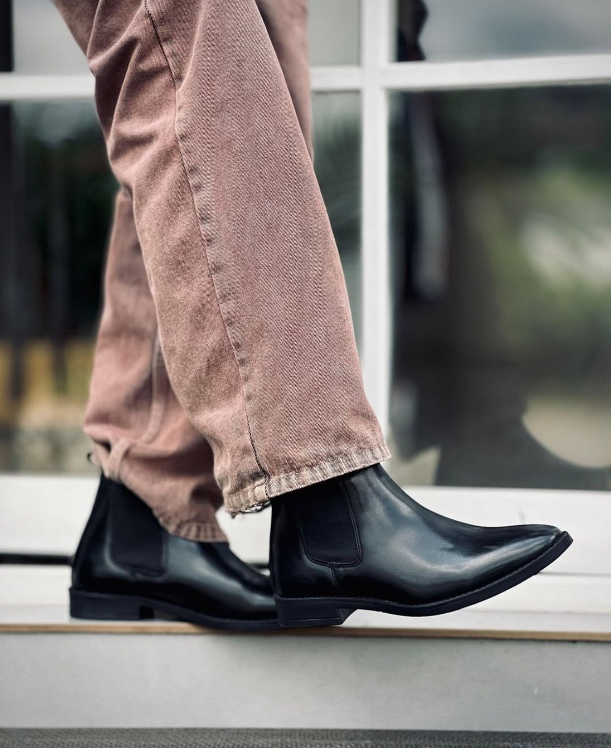 Person wearing black Chelsea leather boots and beige pants on a blurred background