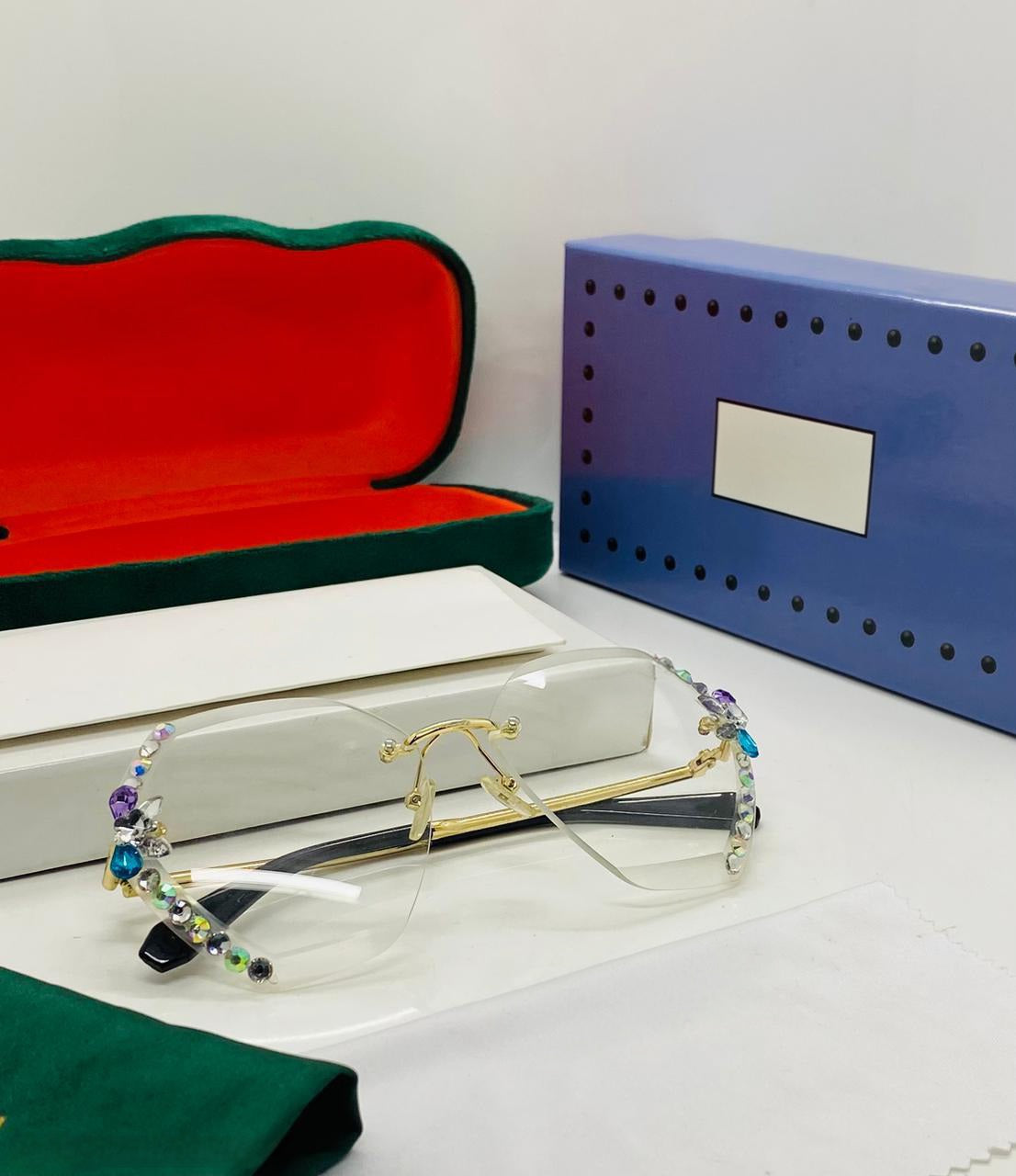 Rimless glasses being held, showing the intricate front view of the crystal work and gold detailing.