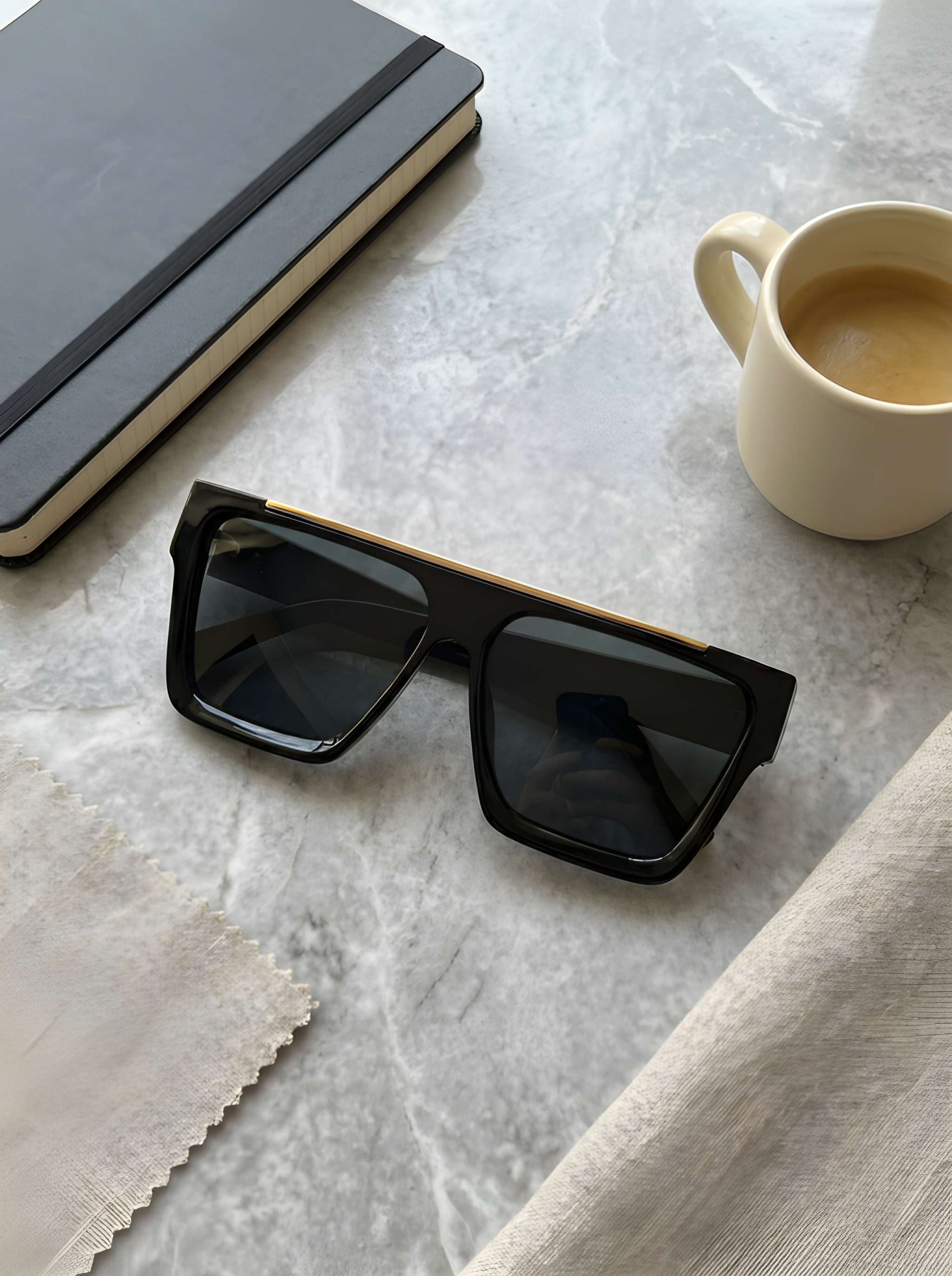 Stylish oversized black sunglasses placed on luxury desk setup with coffee mug