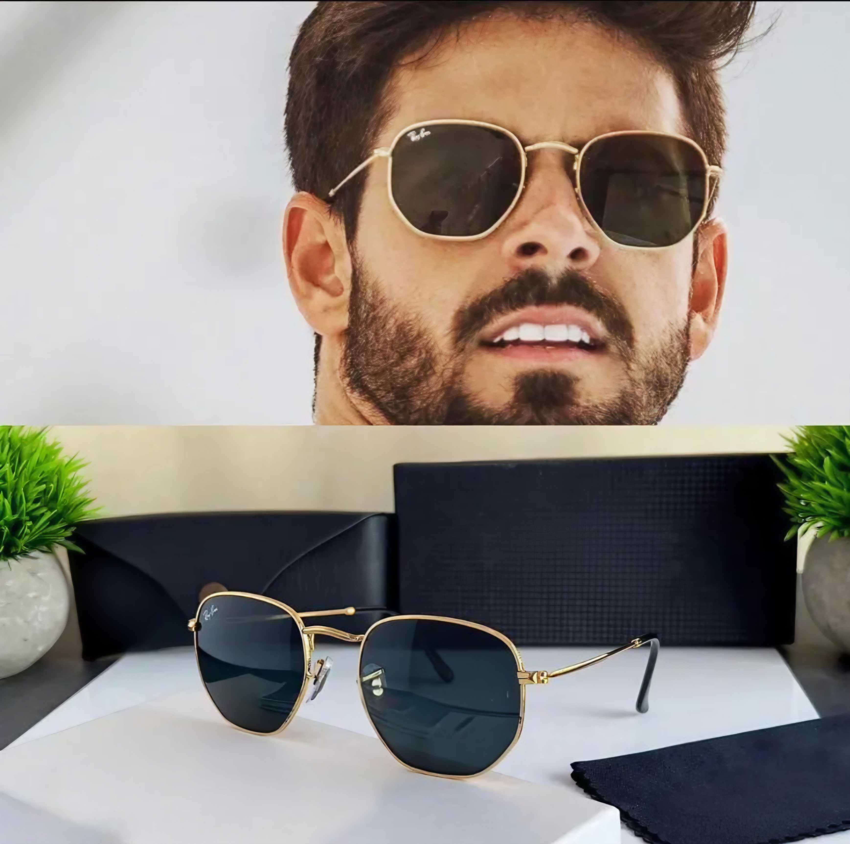 Sunglasses with gold frame and dark lenses displayed on a white surface with a black box and green plants in the background.