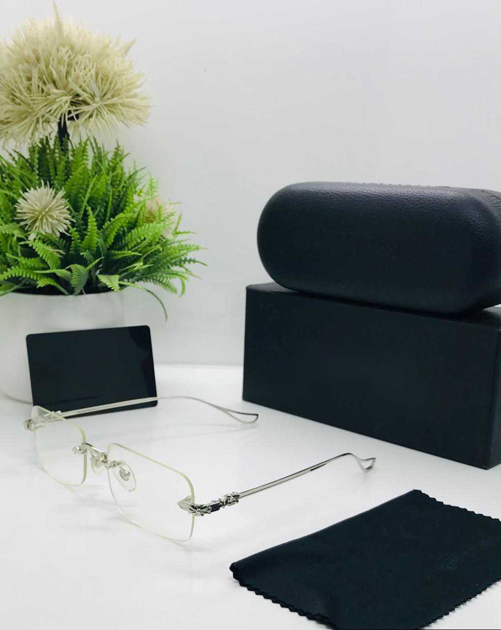 Silver rimless eyeglasses displayed on a white table with a black case and cleaning cloth.